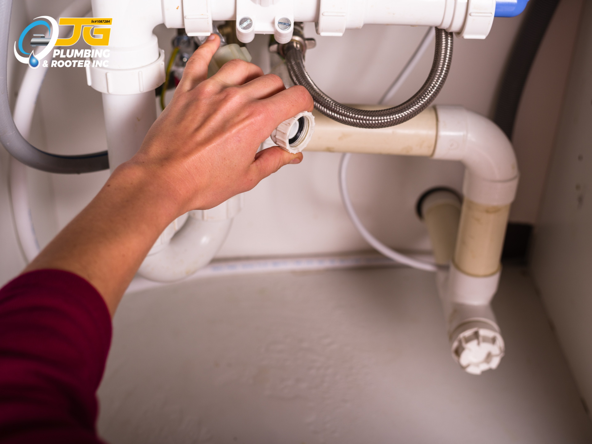 A close-up shot of a hand tightening a white plastic slip nut on PVC plumbing pipes under a sink.